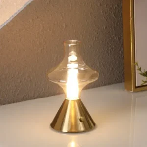 Lampe de chevet en verre vintage et laiton doré allumé sur un bureau.